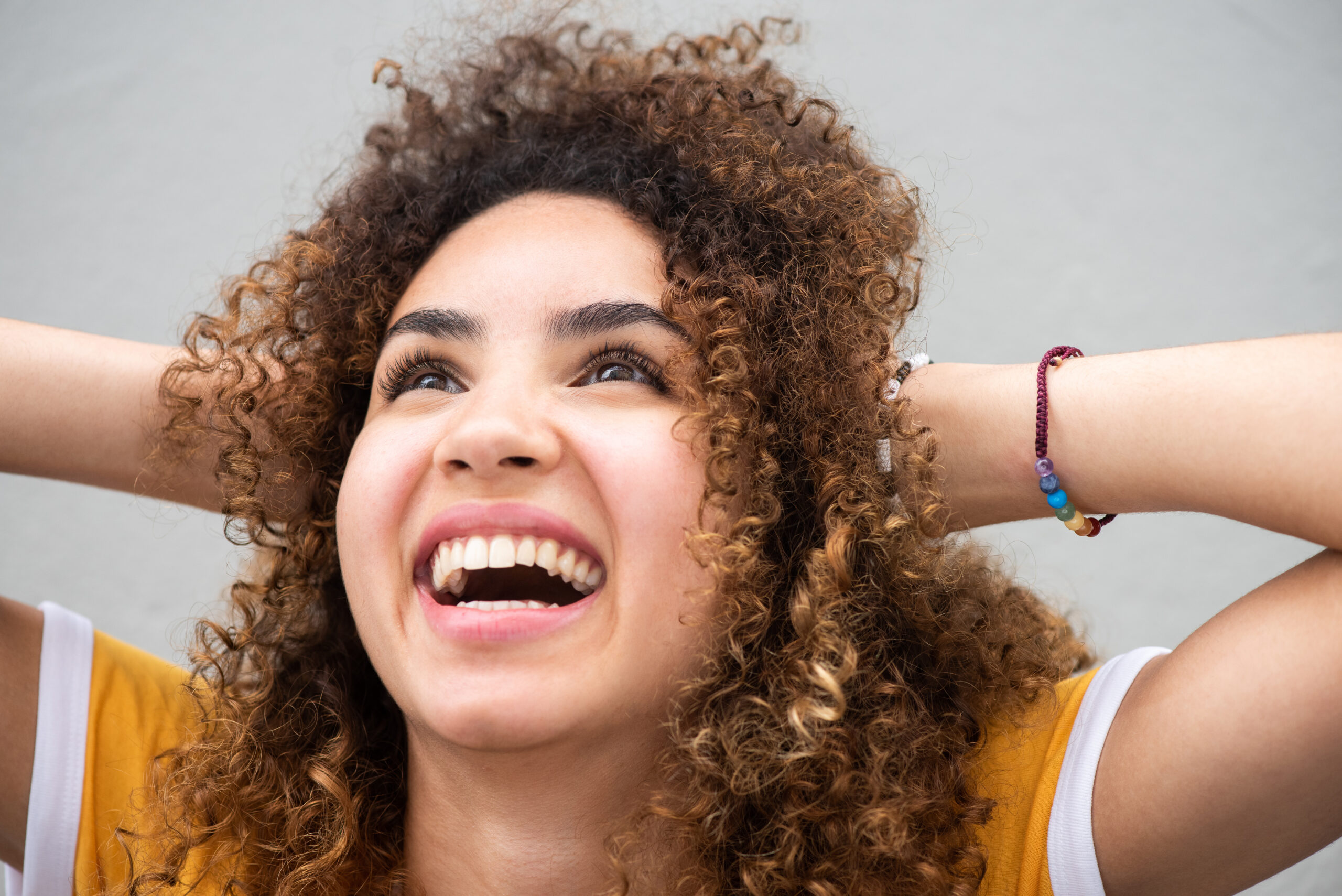 Close up portrait happy smiling young woman with hands in curly hair and looking up