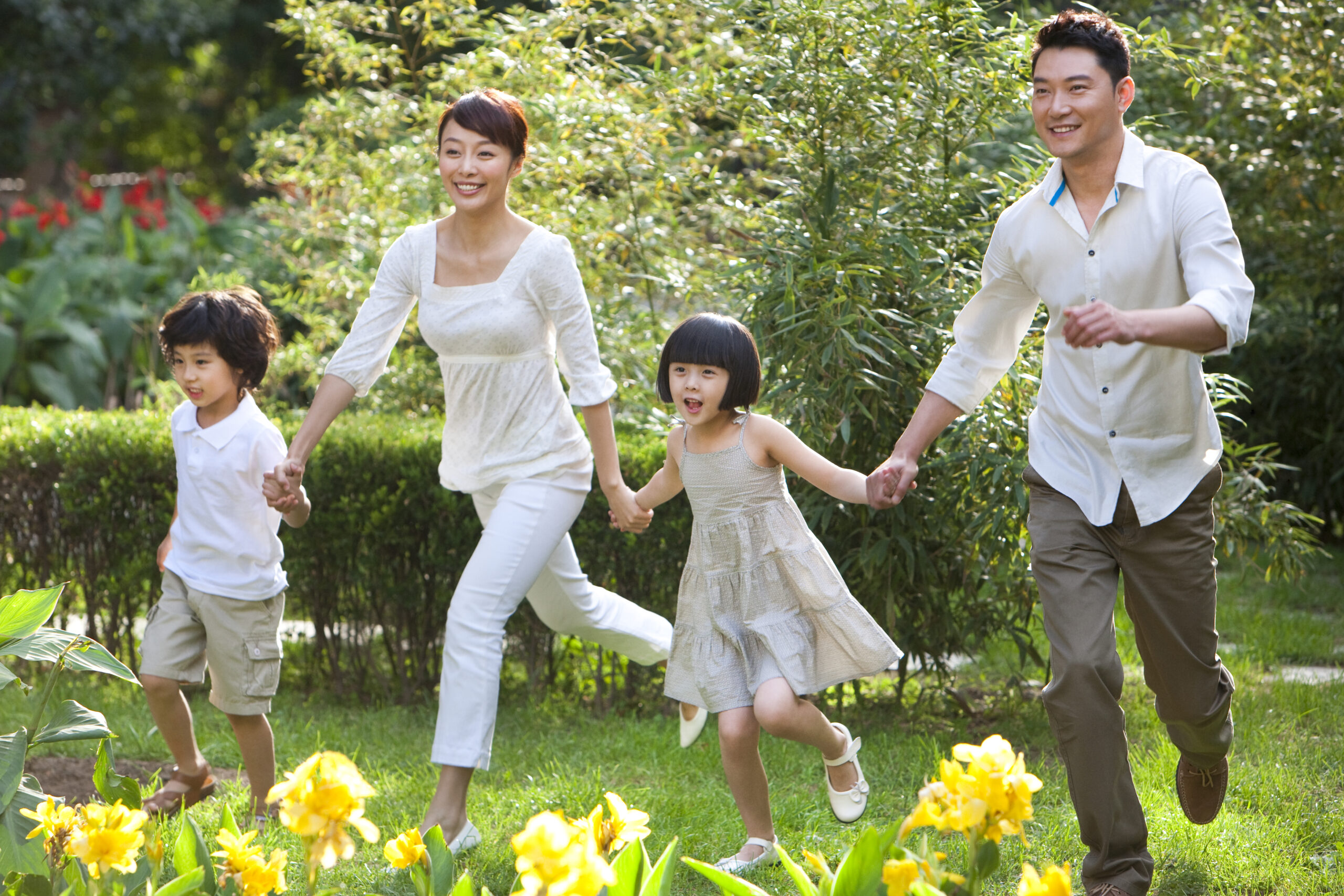 Asian family (parents with two kids) having fun in garden - running and posing for the camera.