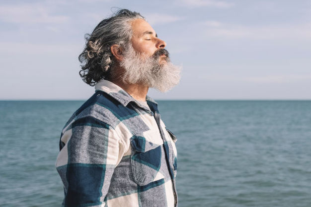 Side view portrait of a bearded man breathing fresh air by the shore